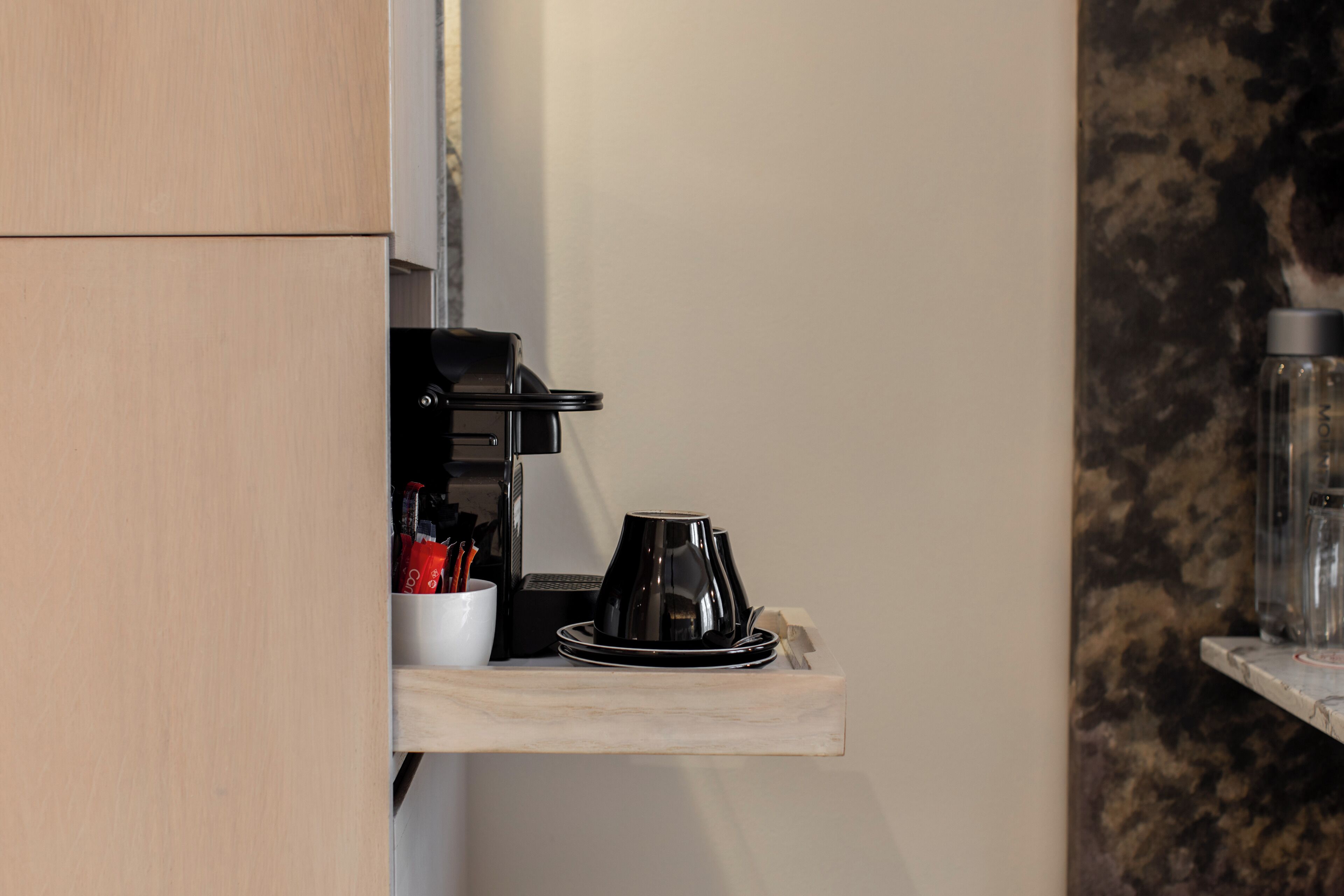 A kitchen area with a coffee machine, a cup, and a water bottle on a shelf.