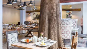 A dining area with a large tree trunk, wooden chairs, a table with plates and a teapot, and hanging pendant lights.