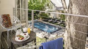 A balcony with a table set for breakfast, overlooking a swimming pool and a tree. - Oude Werf Hotel (Stellenbosch)