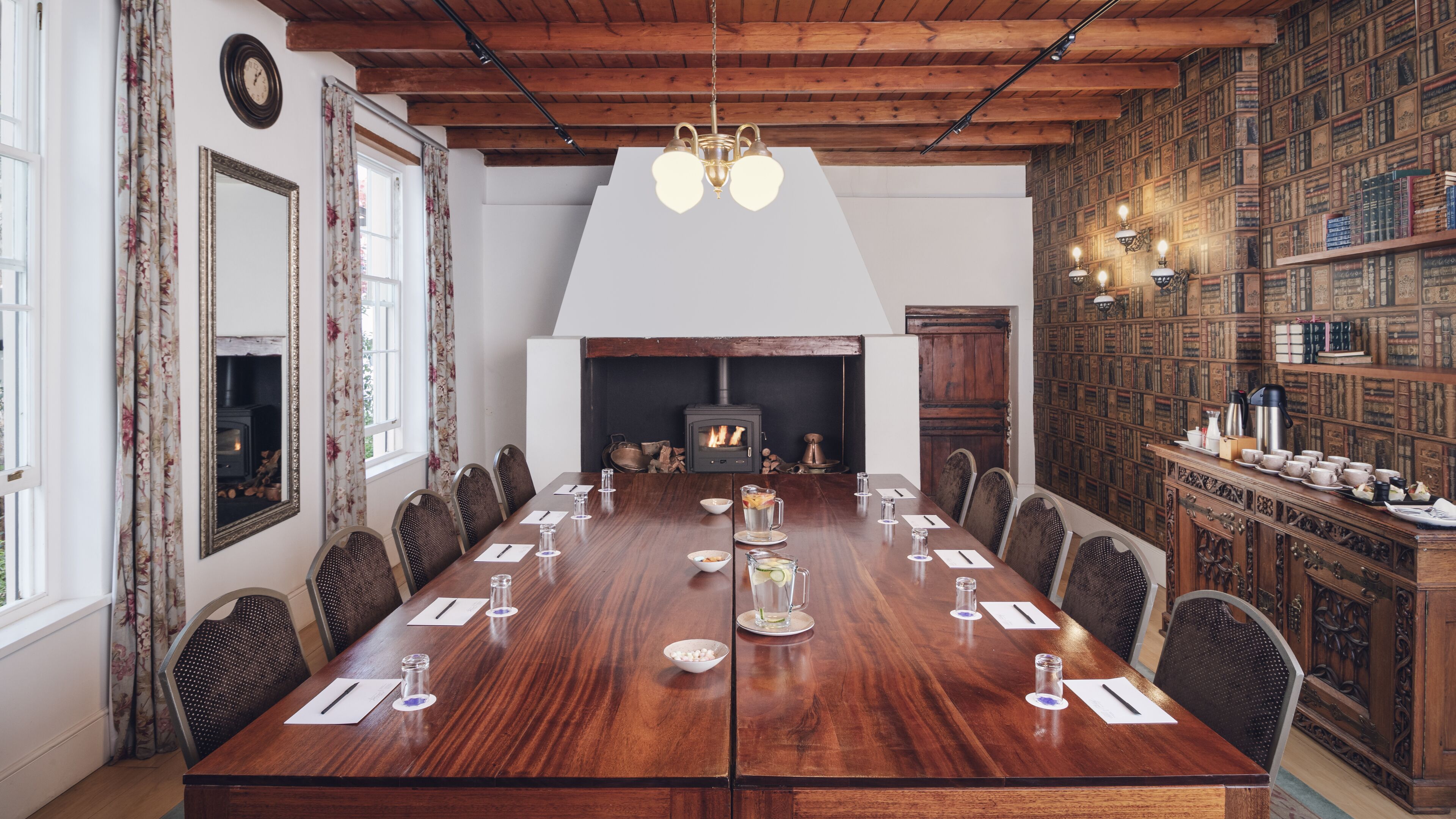 A conference room with a long wooden table, chairs, a fireplace, and a bookshelf filled with books.