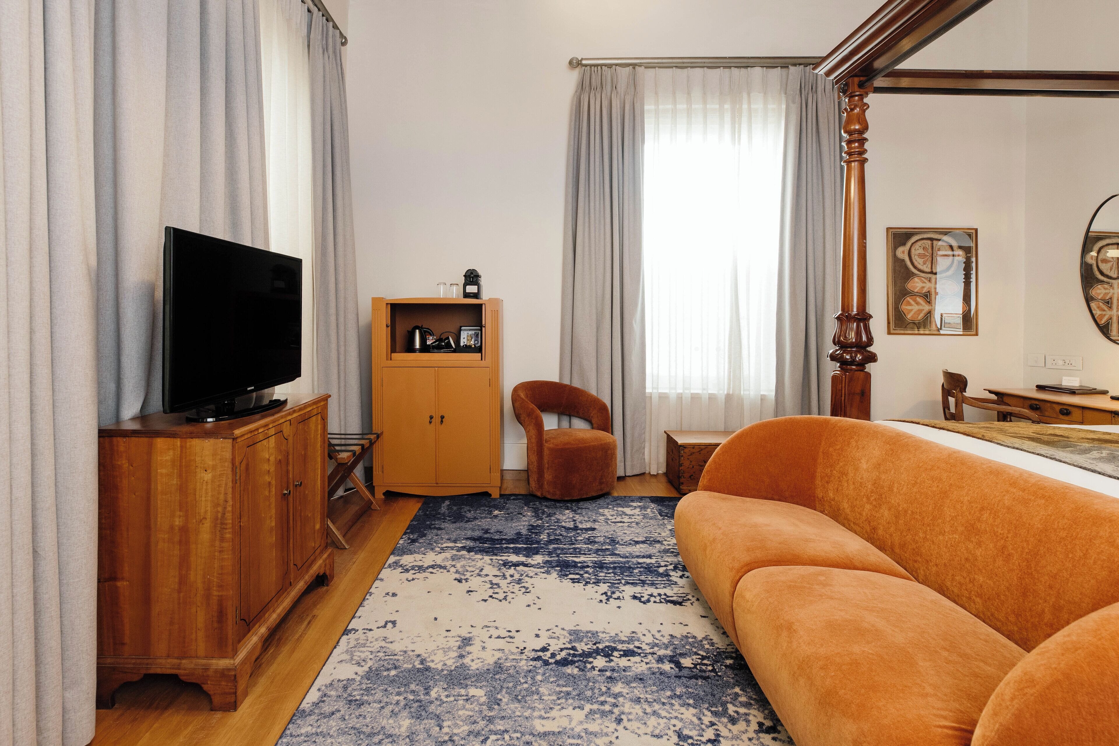 Una sala de estar con televisor, aparador de madera, sofá naranja y alfombra azul estampada.