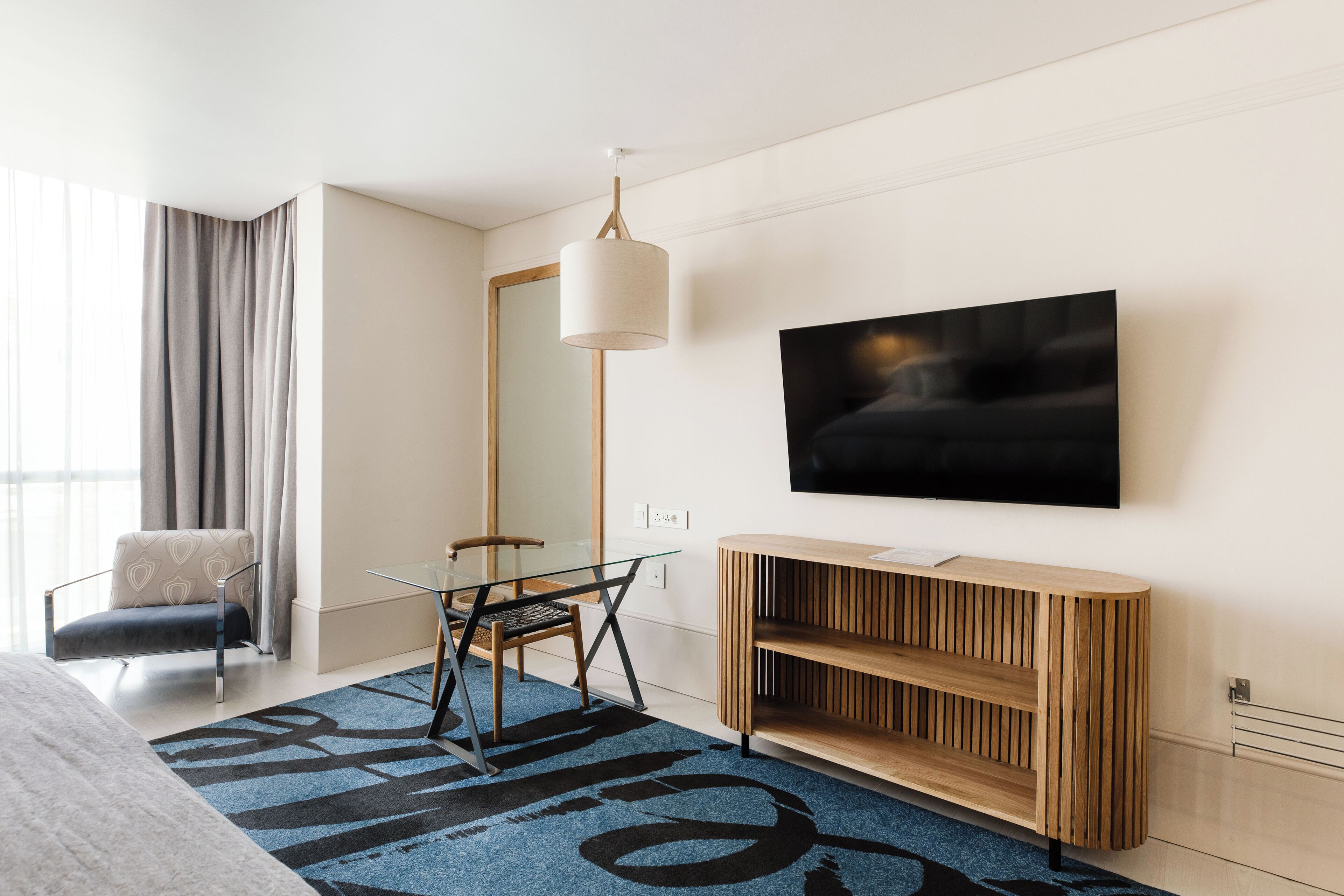 Une chambre d’hôtel moderne avec un grand lit, une table en verre, une chaise, un téléviseur fixé au mur et une console en bois.