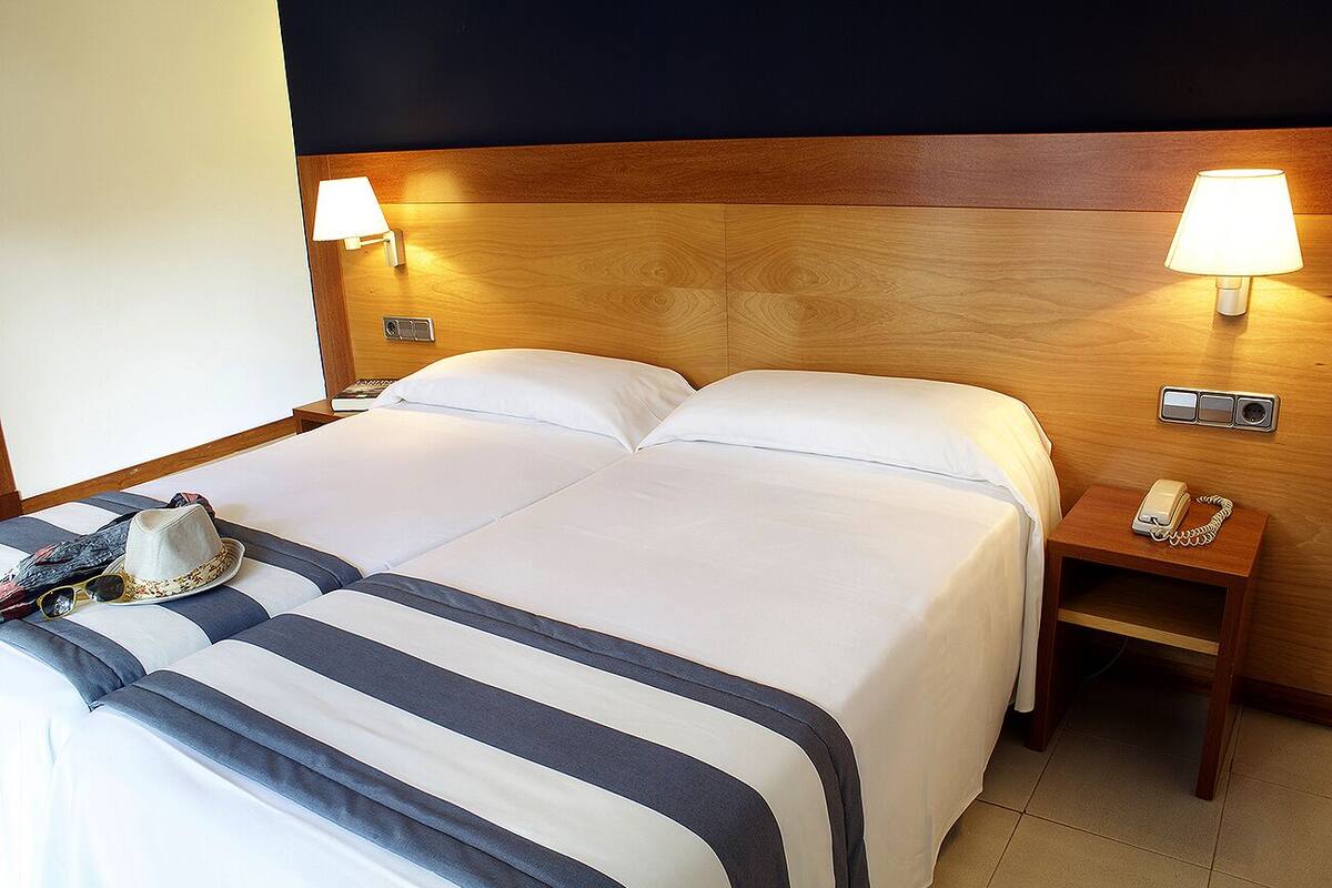Ein Hotelzimmer mit einem großen Bett, zwei Nachttischlampen, einem Telefon am Nachttisch und einem Hut auf dem Bett.