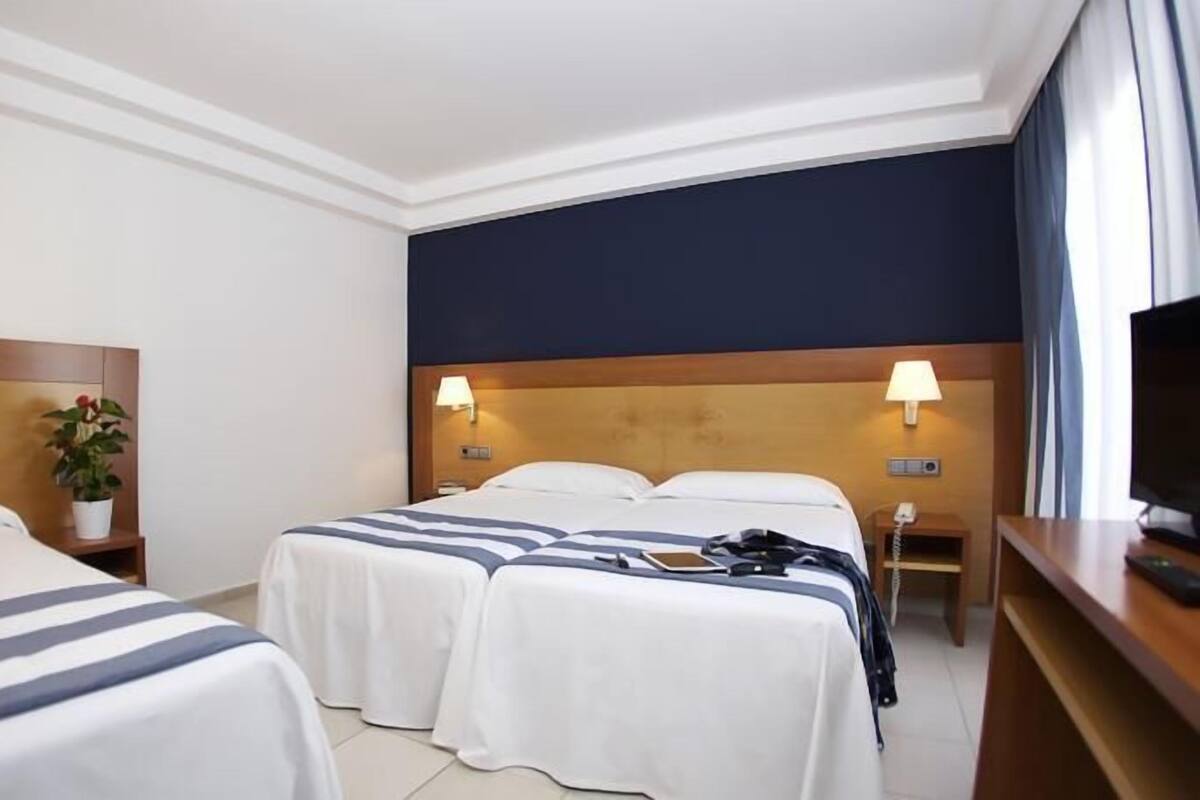 Ein Hotelzimmer mit zwei Betten, einem Fernseher, einem Schreibtisch und einem Nachttisch mit einer Lampe.
