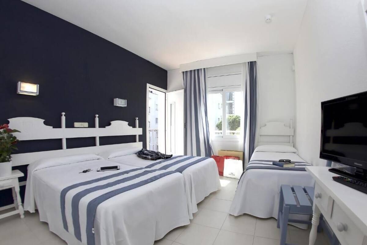 Ein Hotelzimmer mit zwei Betten, einem Schreibtisch mit Fernseher und einem Fenster mit Vorhängen.