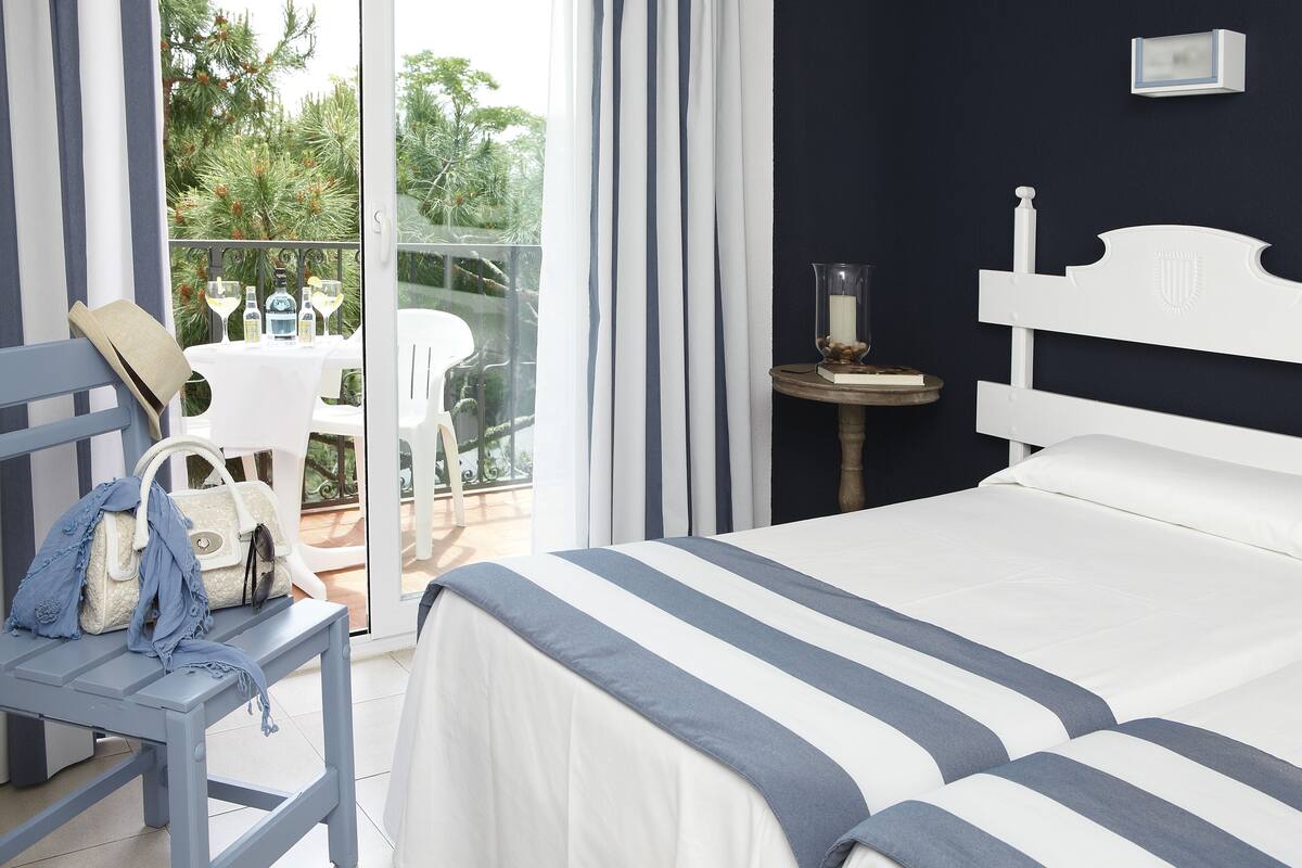 Ein Schlafzimmer mit Bett, Nachttisch, Sessel und Blick ins Freie.