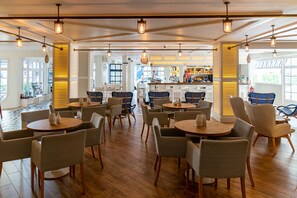 A spacious cafe with multiple seating areas, wooden floors, and hanging light fixtures. - Hotel Els Pins (Castell-Platja d'Aro)