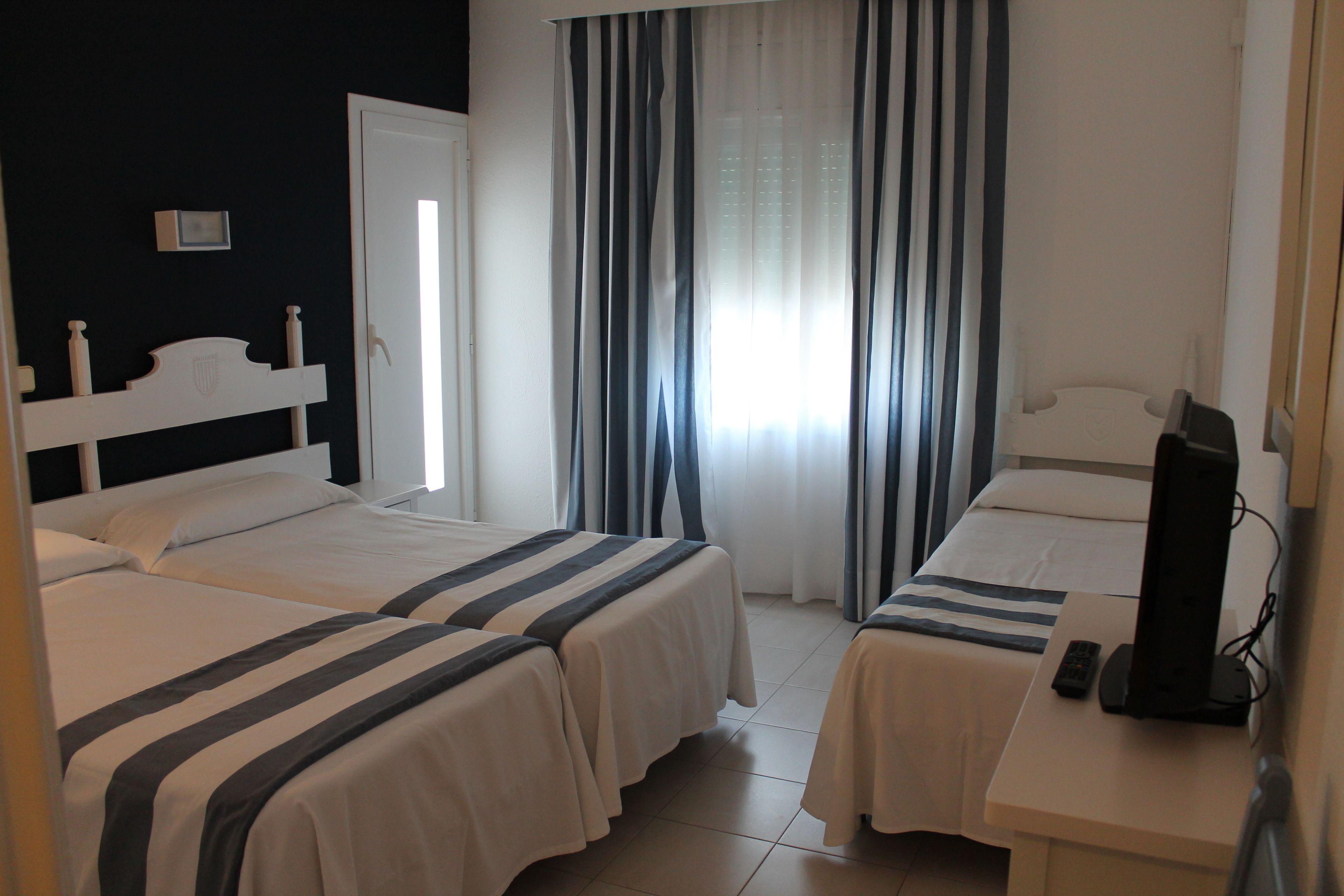 Une chambre d’hôtel avec deux lits, une télévision et une fenêtre avec des rideaux.