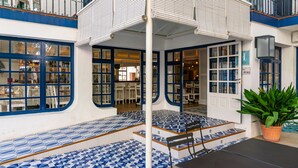 Un área de estar al aire libre techada con baldosas azules y blancas estampadas, una mesa negra y una planta en maceta.