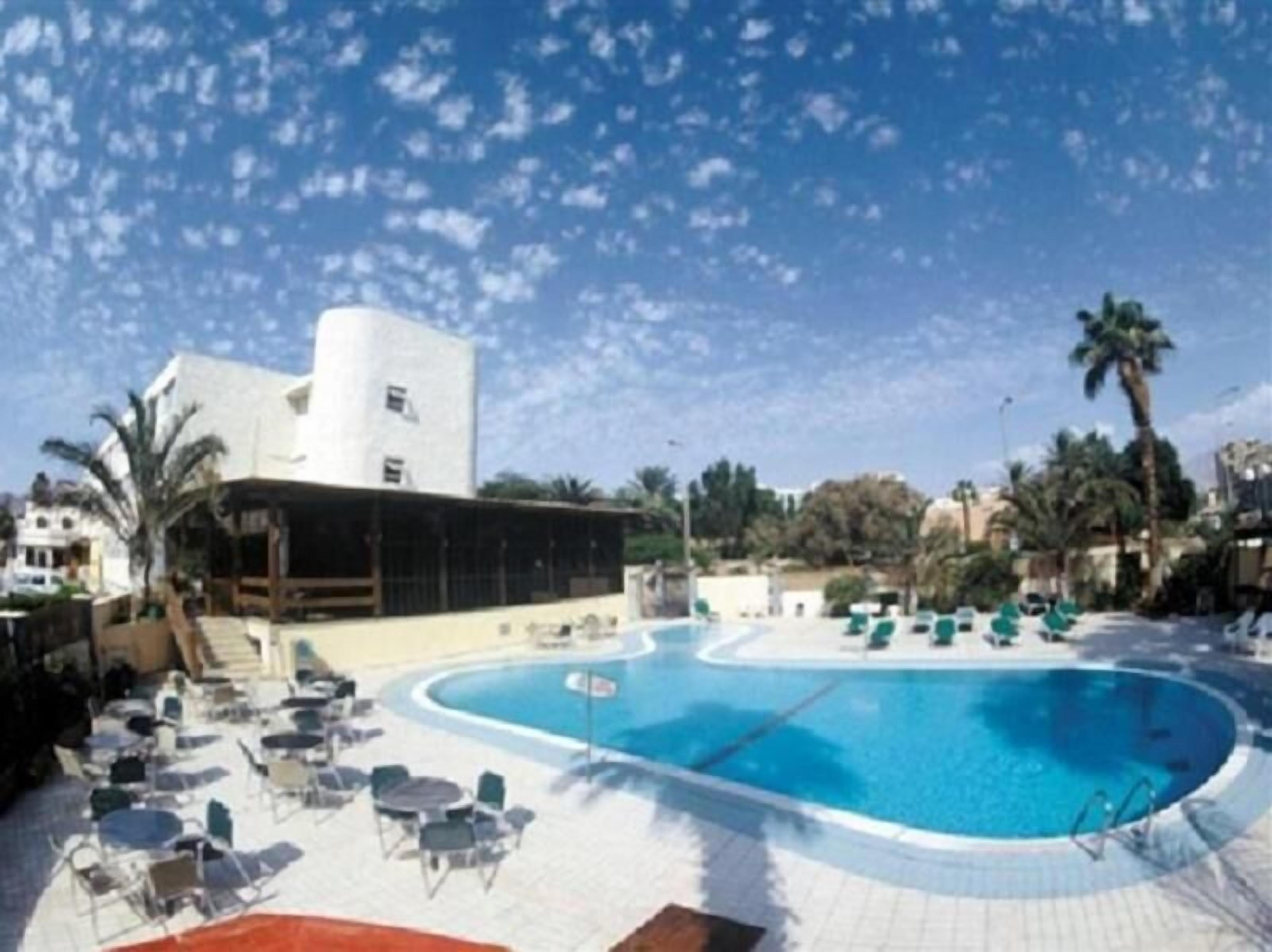 A pool area with lounge chairs and a building with a white facade.
