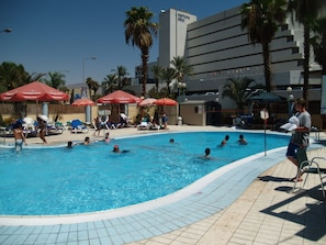 A swimming pool with people swimming and lounging under red umbrellas. - Dalia (EILAT)