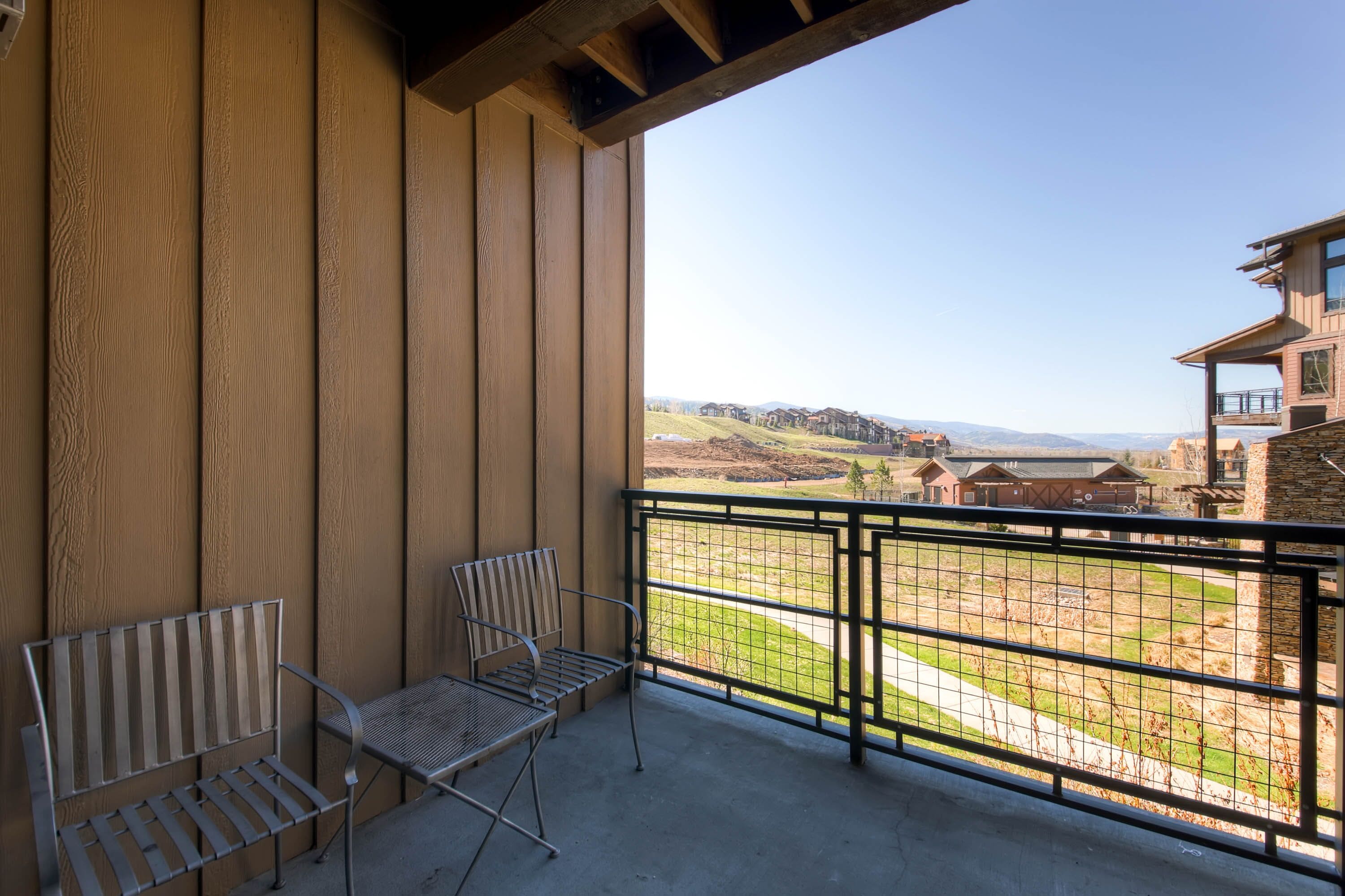 A balcony with two metal chairs and a view of a residential area with houses and a hilly landscape.