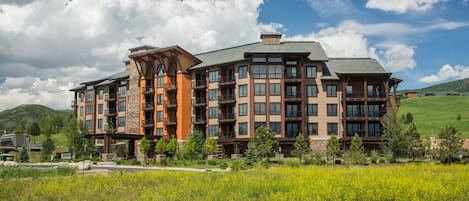 A multi-story hotel with a stone facade, multiple balconies, and a landscaped front yard.