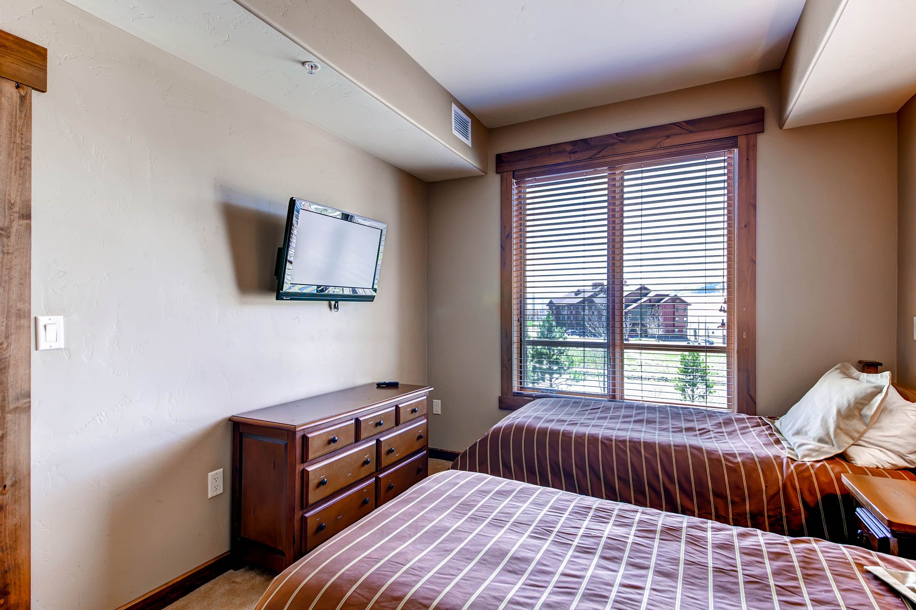A bedroom with two beds, a dresser, a TV, and a window with blinds.