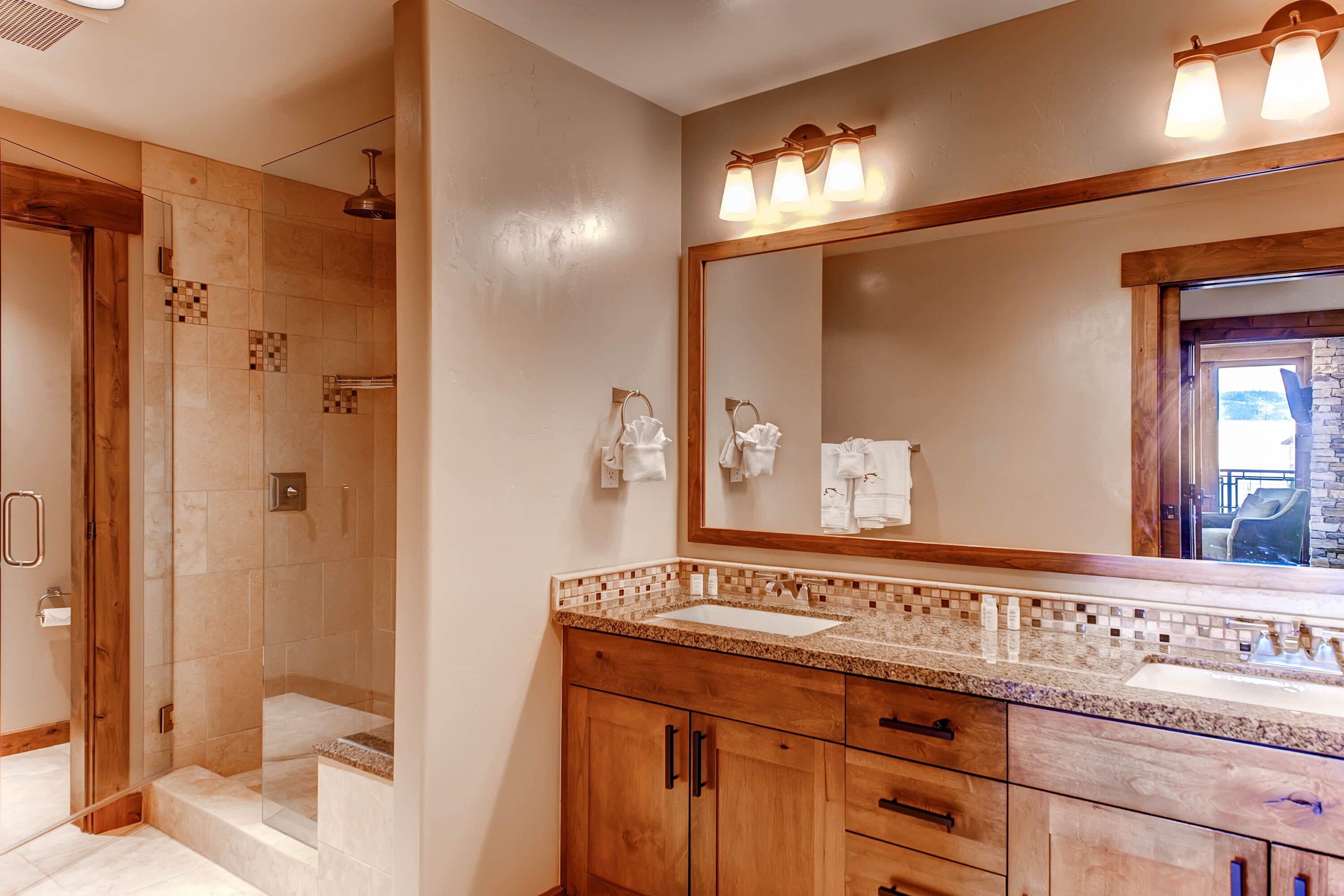 Un baño con ducha, tocador con un espejo grande y un salpicadero de azulejos.
