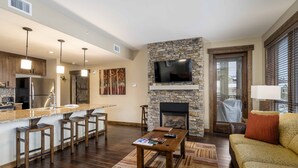 Una sala moderna con chimenea de piedra, televisor montado arriba y zona de bar con taburetes.