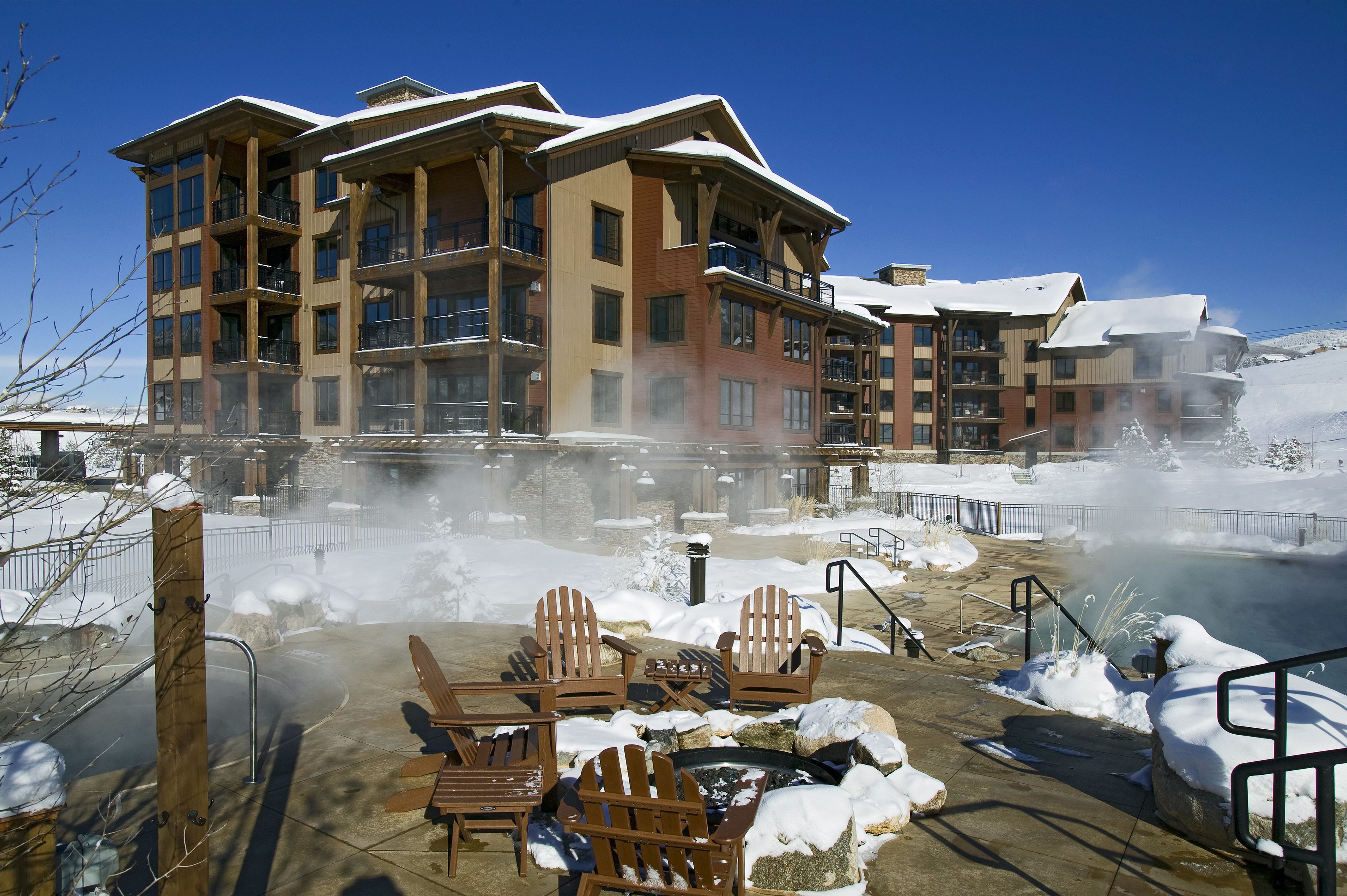 Un hotel a più piani con balconi, un'area idromassaggio con sedie di legno e un paesaggio innevato.
