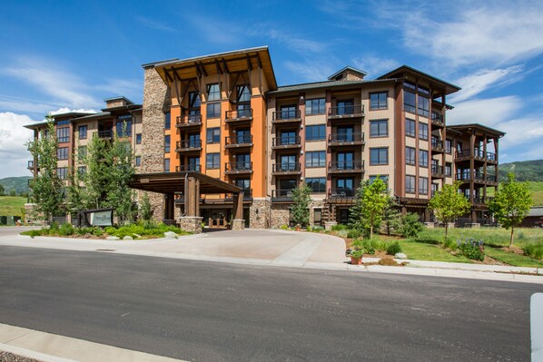 A multi-story hotel with a stone facade, balconies, and a landscaped entrance.
