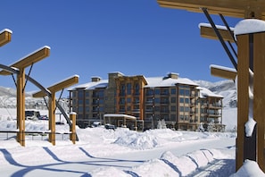 A multi-story hotel with a snow-covered roof and a ski resort in the background.