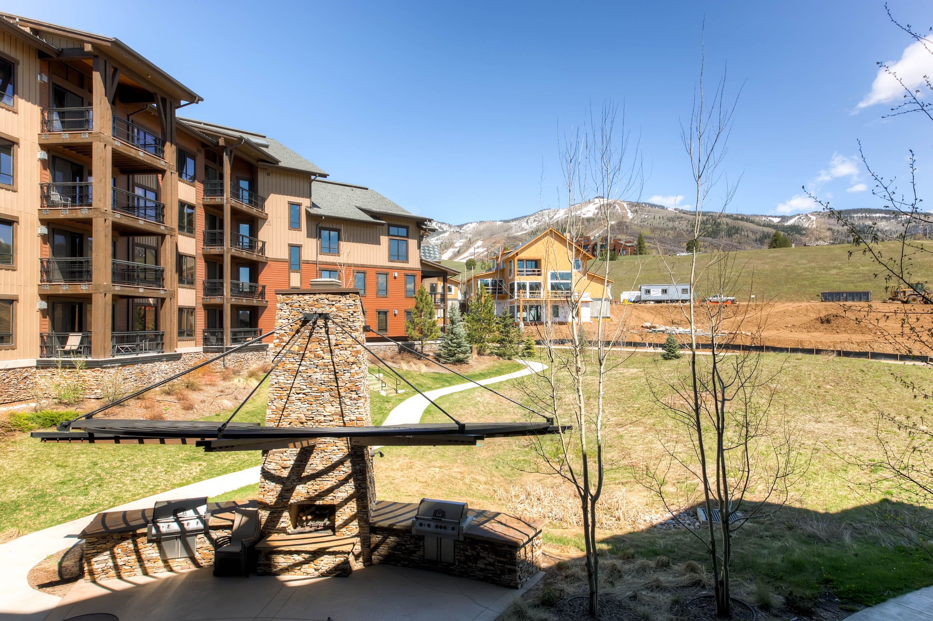 Un hotel moderno con varios pisos, mobiliario exterior y vistas a un paisaje montañoso.
