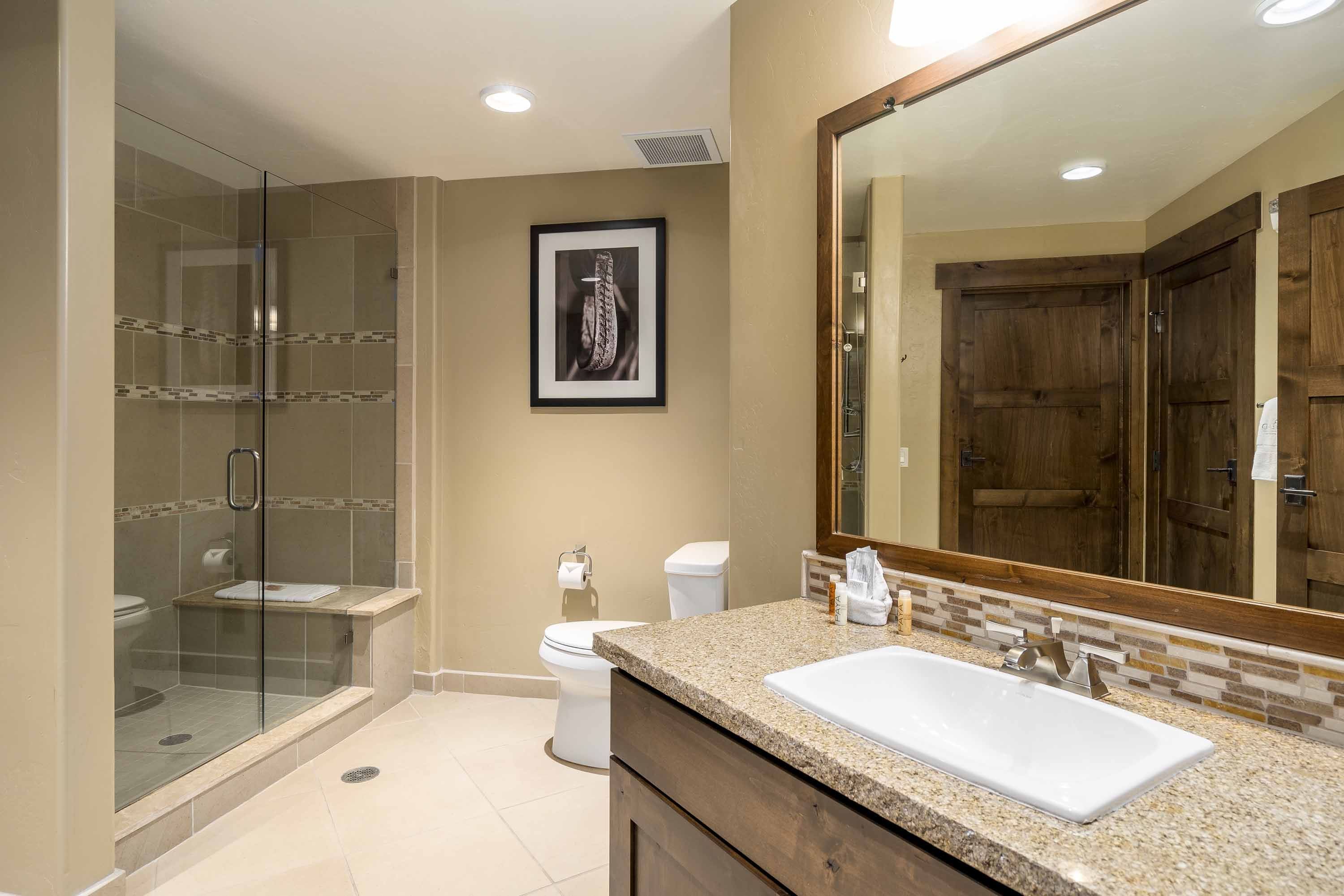 A modern bathroom with a glass-enclosed shower, a large mirror, and a granite countertop sink.