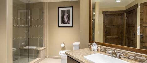 A modern bathroom with a glass-enclosed shower, a large mirror, and a granite countertop sink.