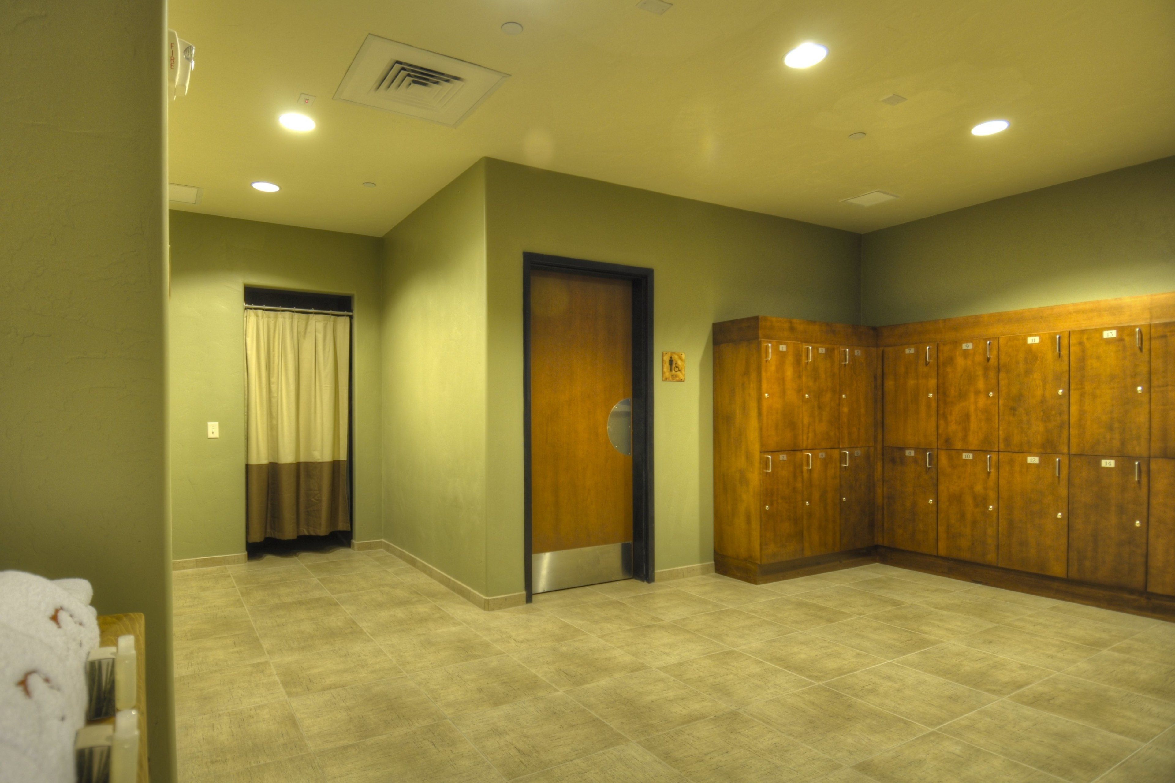 Un vestiaire avec un sol carrelé de couleur beige, des casiers en bois et une porte dotée d’une fenêtre et d’un rideau.