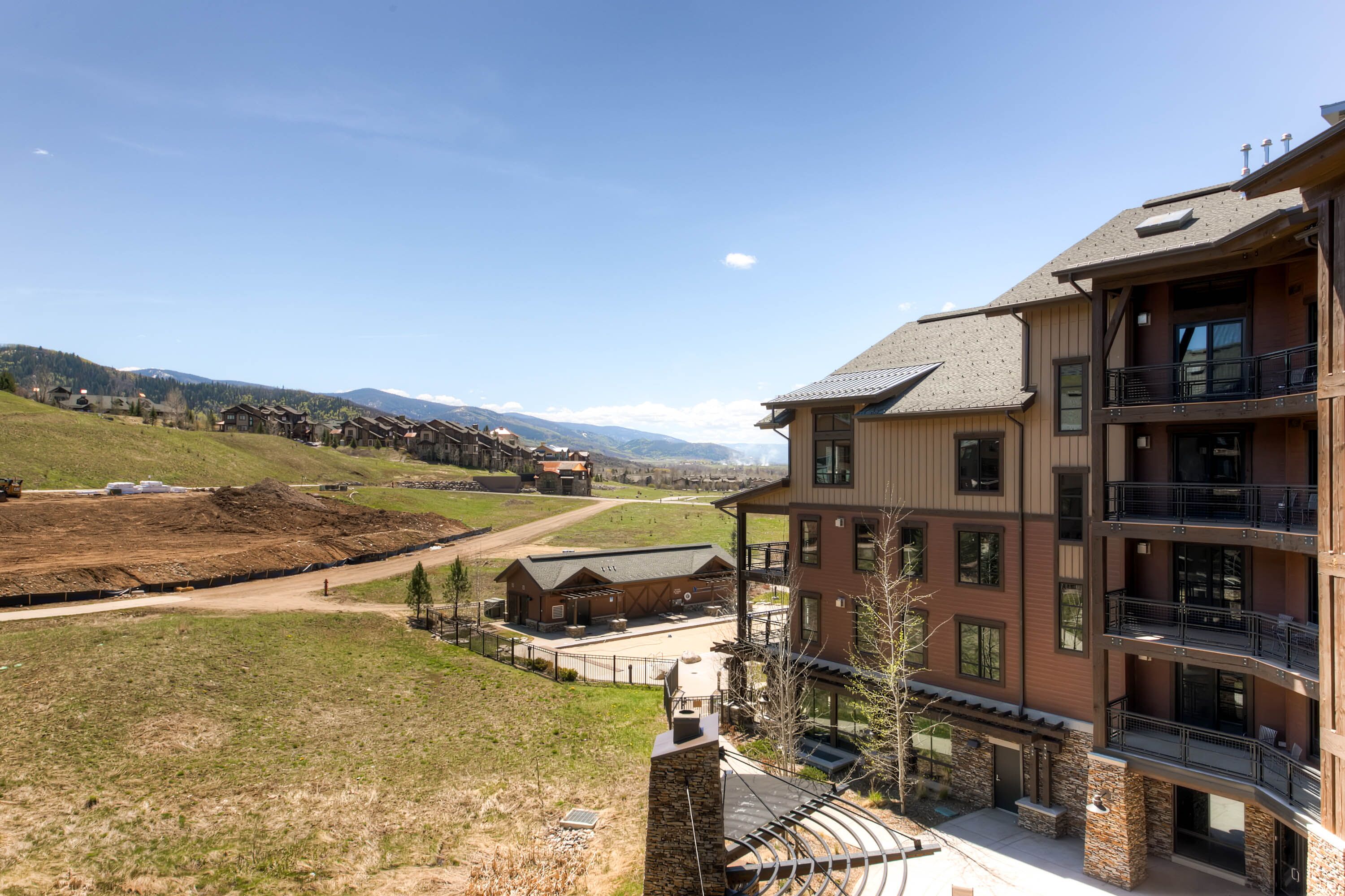 A multi-story building with balconies, a stone facade, and a view of a hilly landscape.