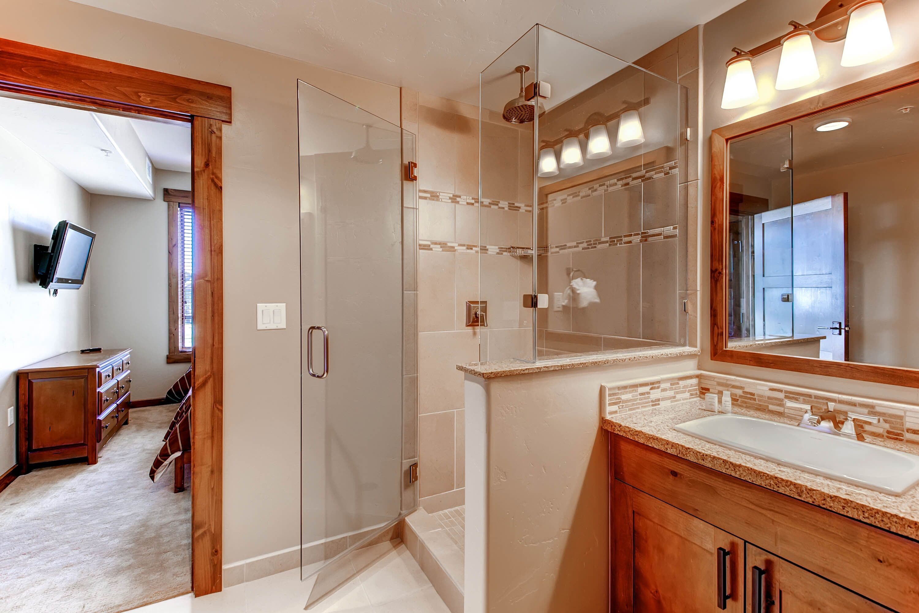 Un baño moderno con cabina de ducha de vidrio, un espejo grande y un lavamanos.