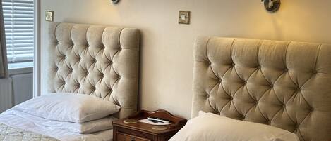 Une chambre d’hôtel avec deux lits, chacun doté d’une tête de lit capitonnée, de tables de chevet, de lampes et d’une fenêtre avec des stores.
