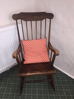 Una silla de madera con un cojín rojo estampado, ubicada frente a un radiador blanco y una alfombra verde con textura.