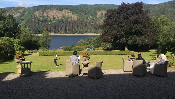 A serene outdoor seating area with wicker furniture overlooking a lake and forested hills. - Dale Head Hall Lakeside Hotel (Keswick)