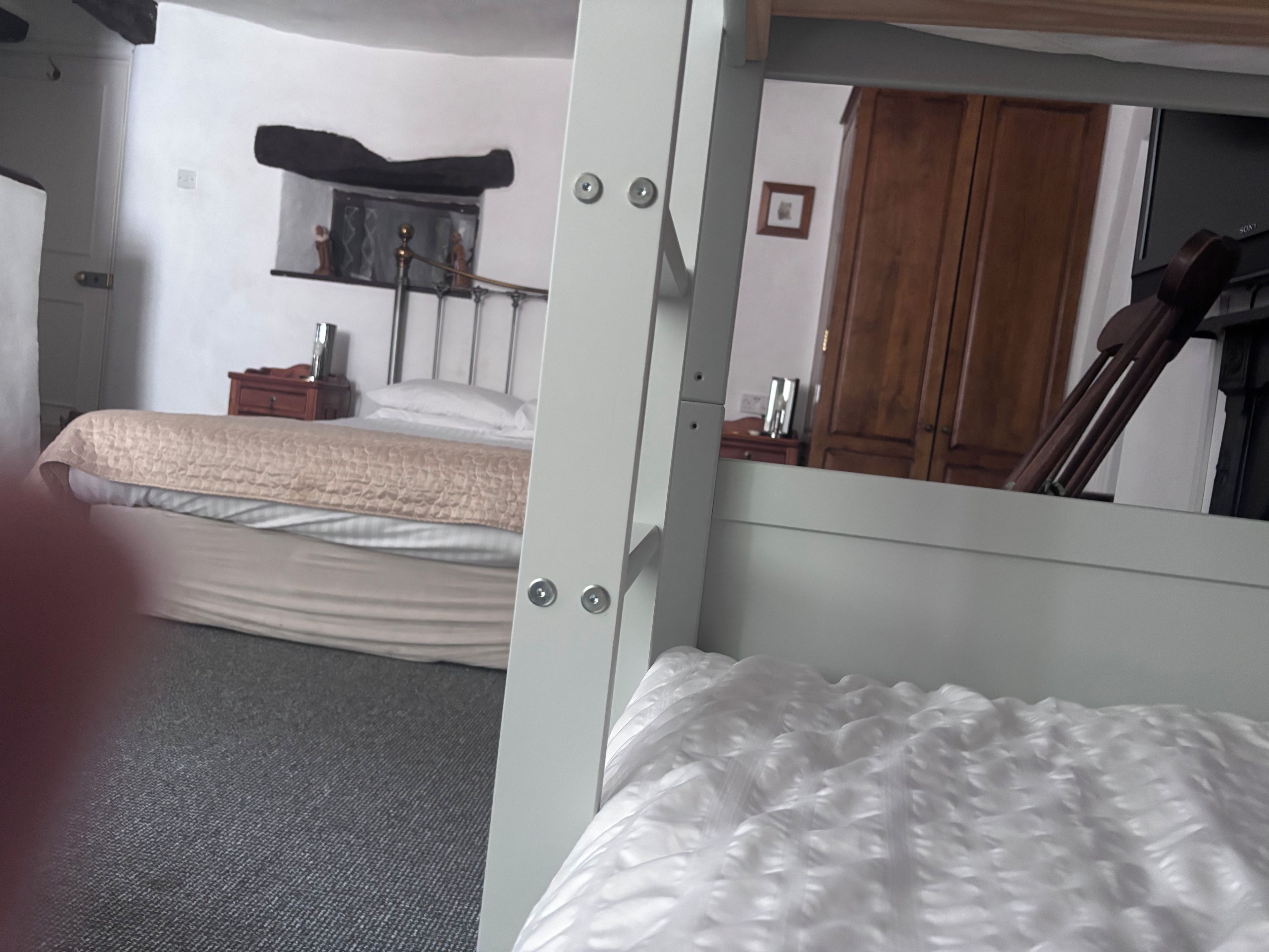 Um quarto com cama de solteiro e beliche, mesa de cabeceira, espelho e guarda-roupa.