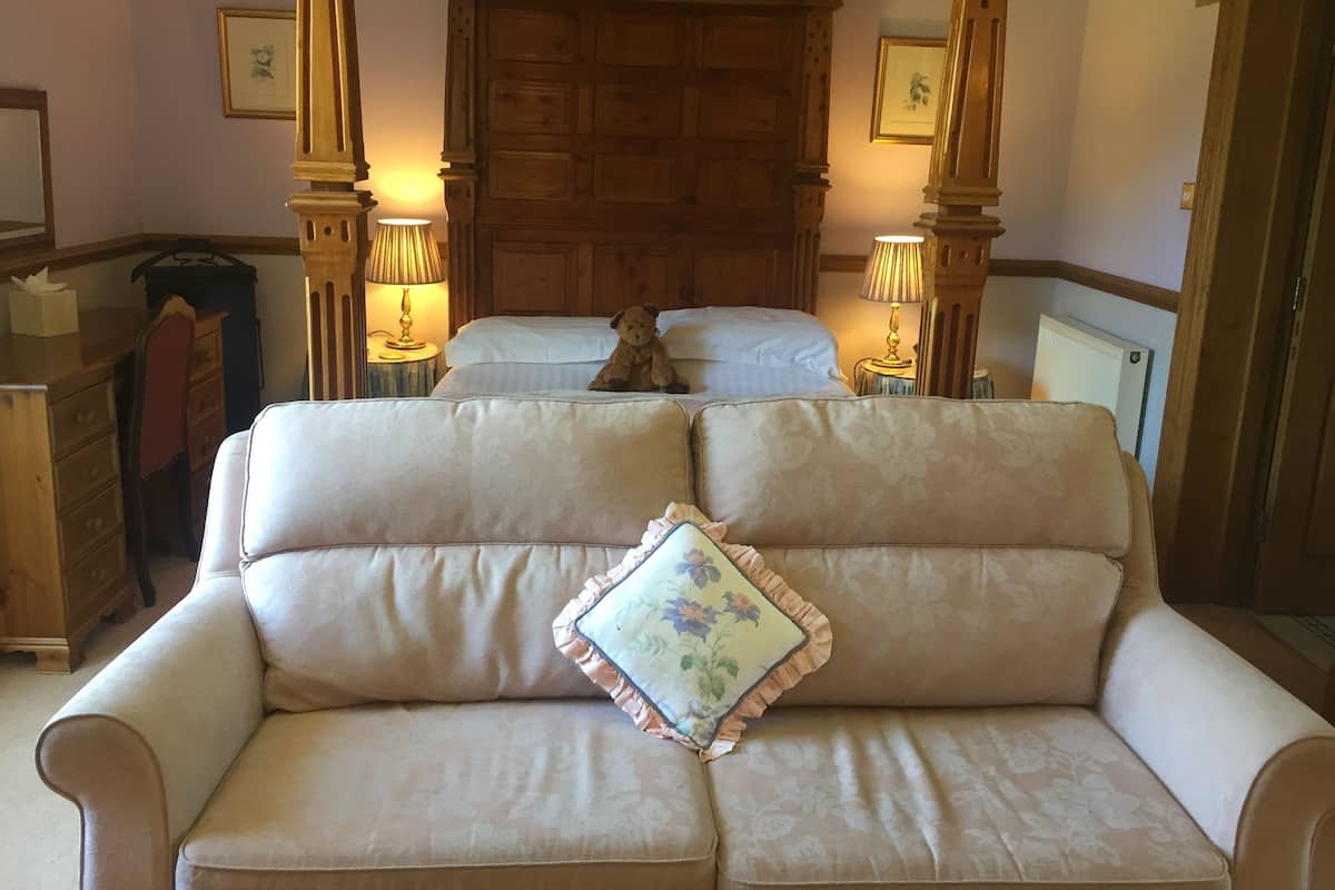 A cozy room with a sofa, two beds, wooden paneling, and lamps.