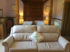 A cozy room with a sofa, two beds, wooden paneling, and lamps. - Dale Head Hall Lakeside Hotel (Keswick)