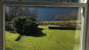A view through a window of a grassy field, a body of water, and a forested hill. - Dale Head Hall Lakeside Hotel (Keswick)