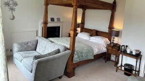 A four-poster bed with a wooden canopy, a grey sofa, and a bedside table with a lamp and a kettle. - Dale Head Hall Lakeside Hotel (Keswick)