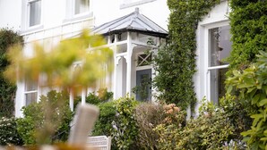 A white building with a covered porch and lush greenery. - Dale Head Hall Lakeside Hotel (Keswick)