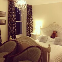 Un dormitorio con cama, mesita de noche, lámpara, un osito de peluche y un candelabro.