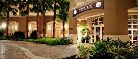 A hotel entrance with a sign reading "MARKER 92 Waterfront Bar & Restaurant," palm trees, and a brick pathway.