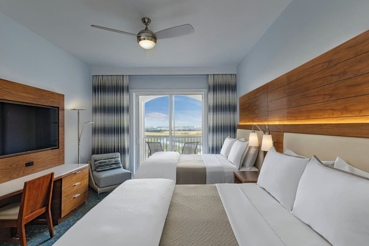 Quarto de hotel com uma cama grande, uma escrivaninha, uma televisão e varanda com vista.
