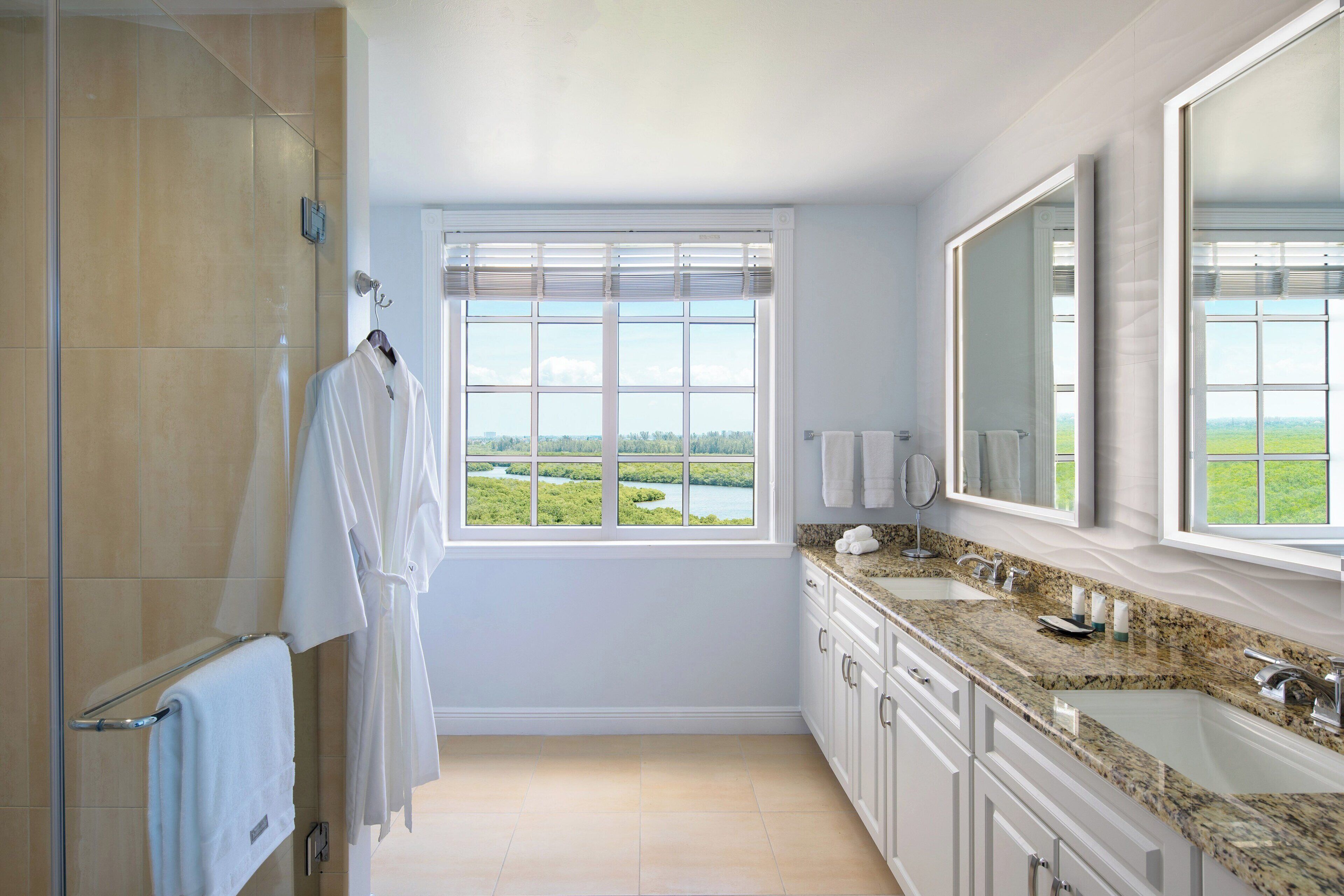 A modern bathroom with a large window, a walk-in shower, and a granite countertop sink.