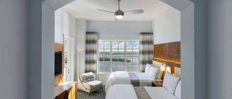 A hotel room with two beds, a desk, a chair, a TV, and a view of the water.