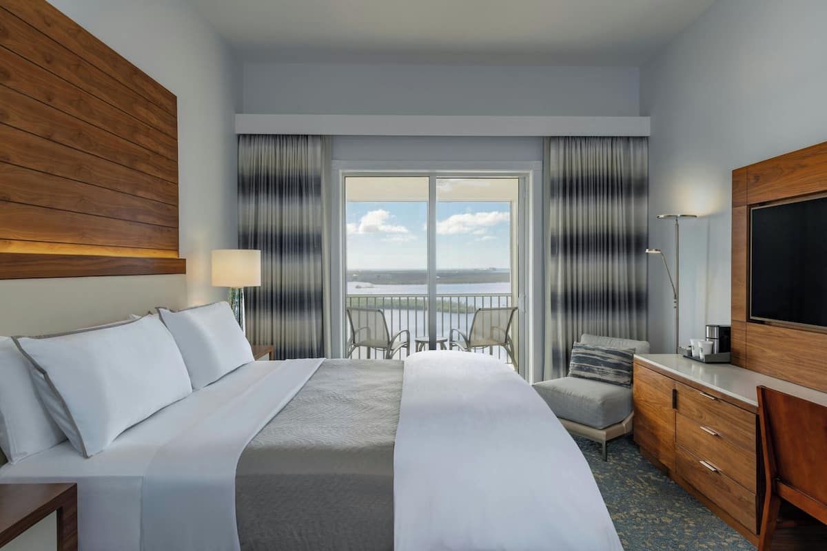 Quarto de hotel com uma cama grande, uma escrivaninha, uma cadeira, televisão e varanda com vista.