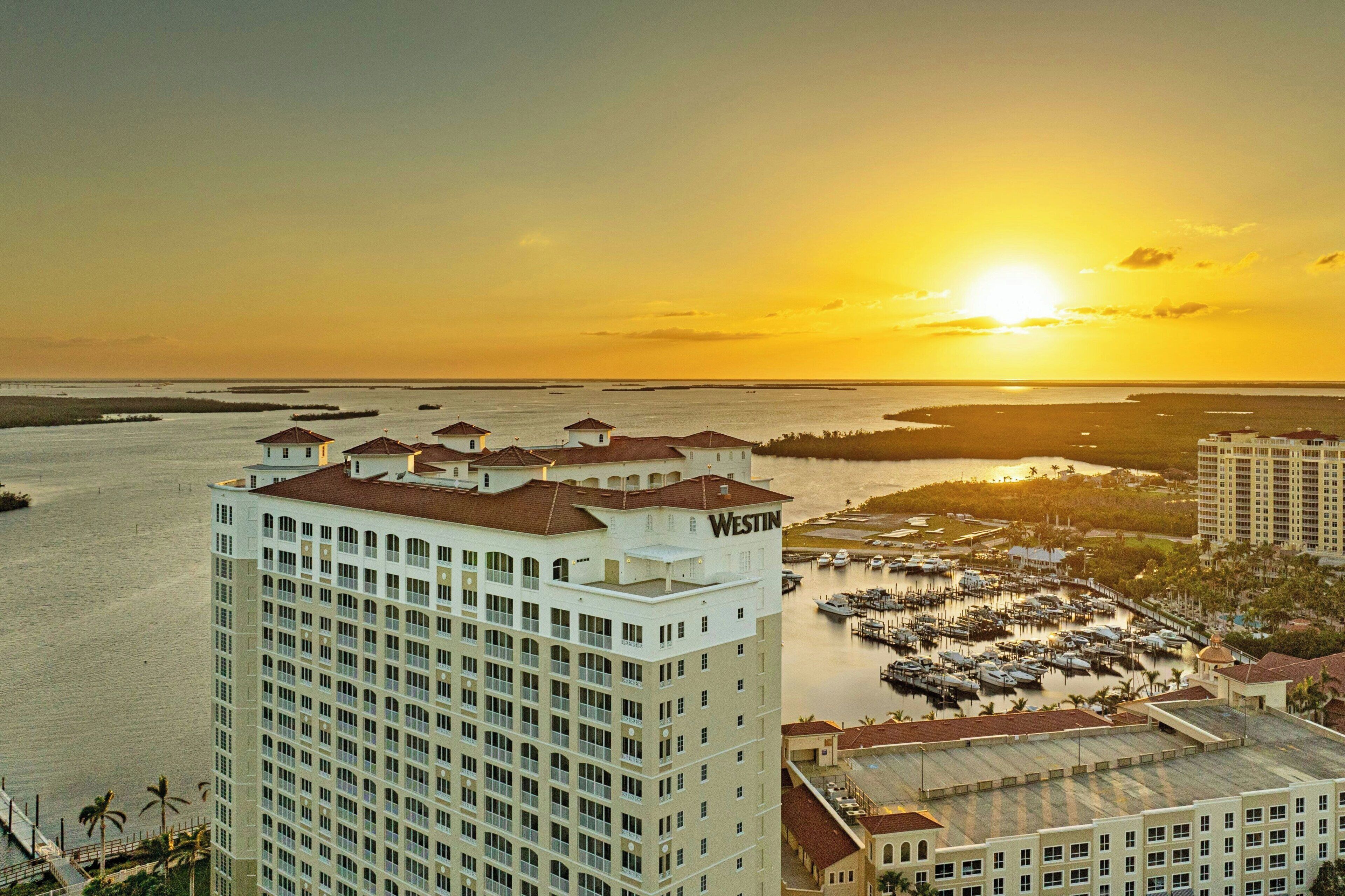 A high-rise hotel with a marina and boats, surrounded by water and palm trees.