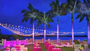 An outdoor seating area with round tables and pink cushions, palm trees, and string lights against a twilight sky. - The Westin Cape Coral Resort At Marina Village (Cape Coral)