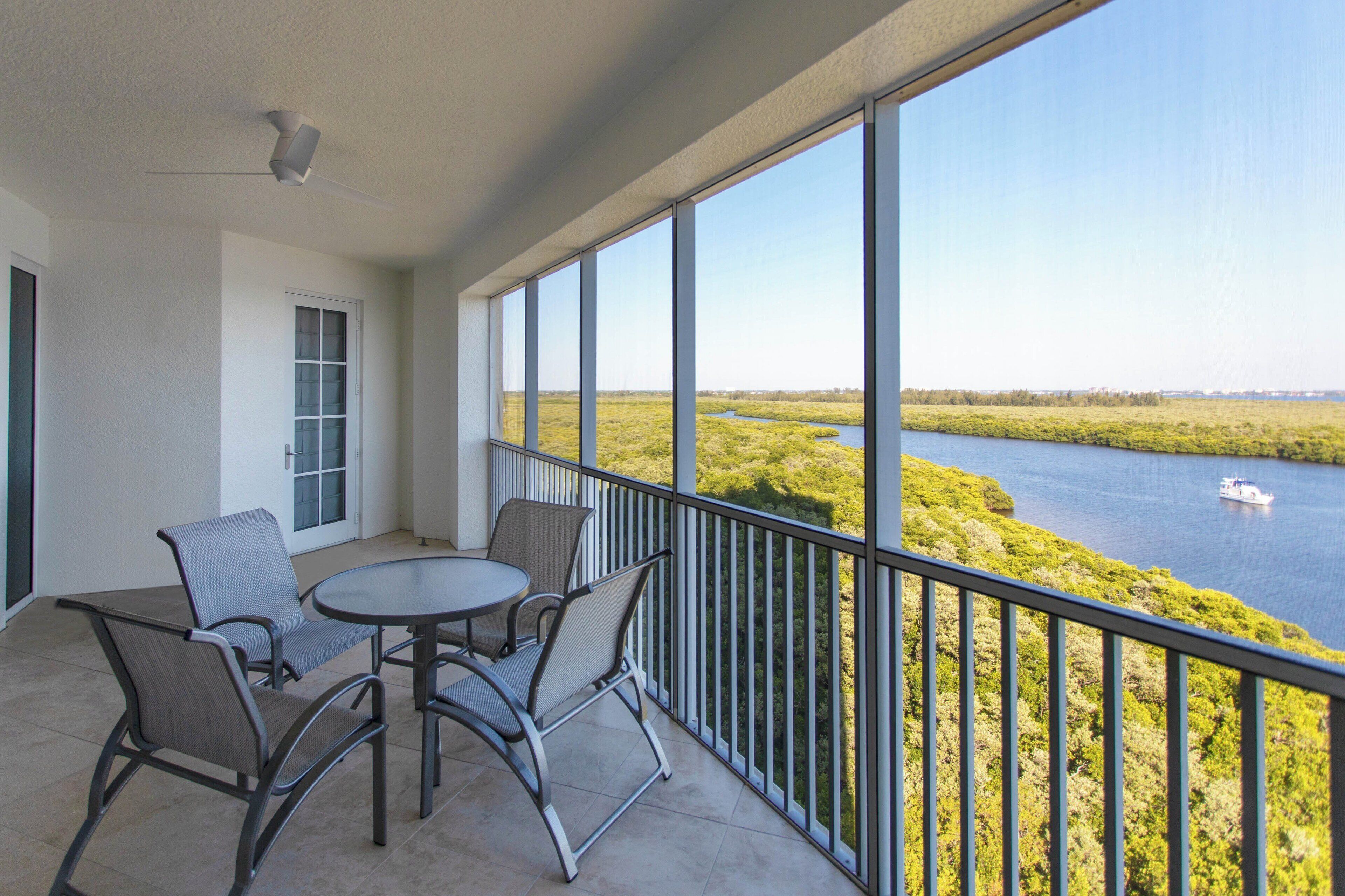 A balcony with a table and chairs, overlooking a body of water and greenery.