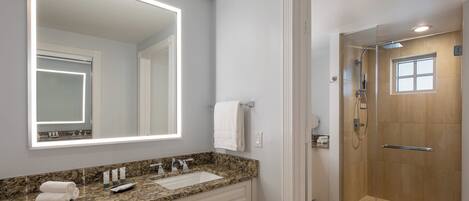 Un baño con encimera de granito, un espejo grande, ducha con cerramiento de vidrio y una toalla blanca en la pared.