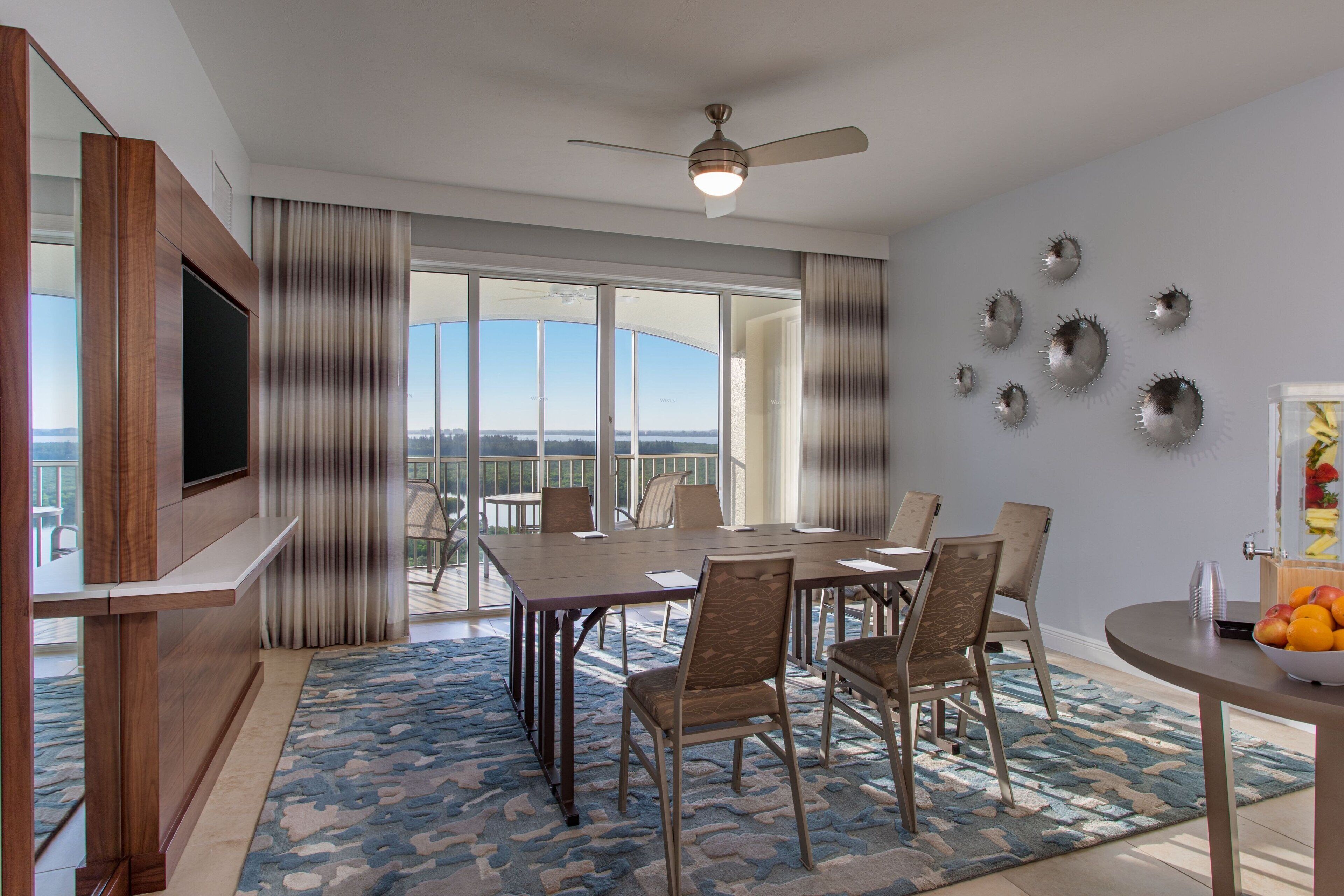 A spacious dining area with a large table and chairs, a ceiling fan, and a view through large windows.