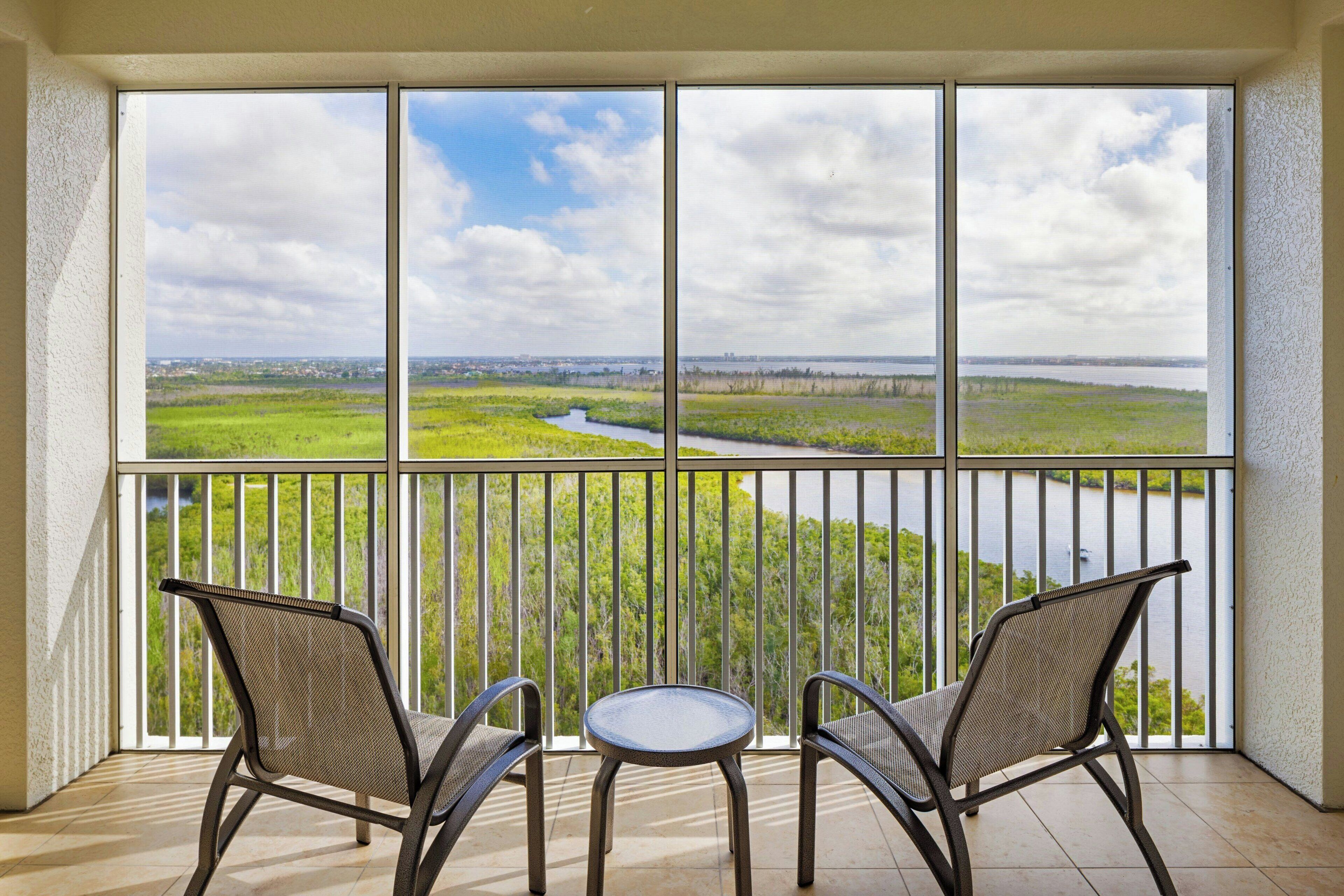Un balcon avec deux chaises et une petite table, donnant sur une rivière et un paysage verdoyant.